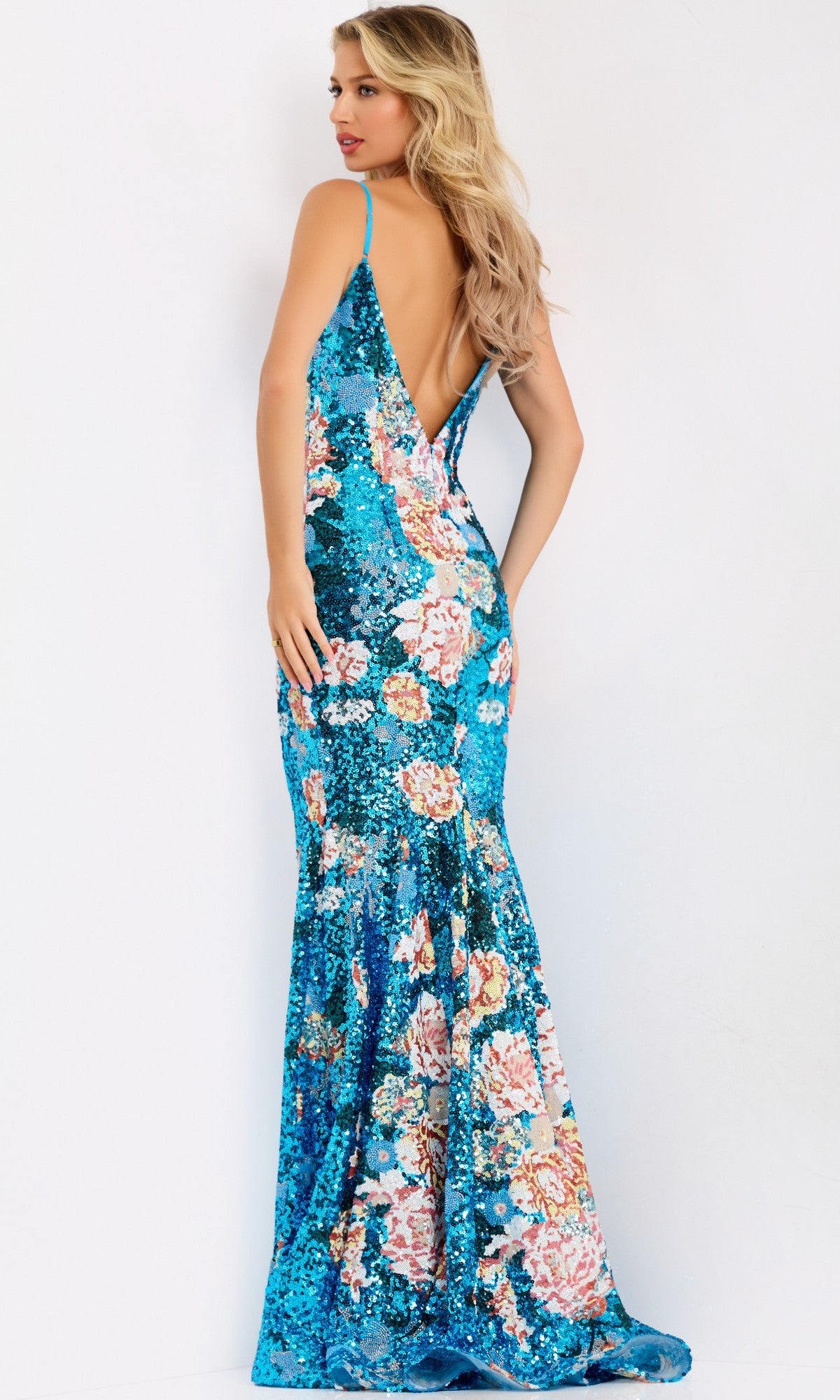 A woman models the Jovani 48637 long prom dress in blue floral sequin with a mermaid silhouette, low back, and thin straps, standing against a plain white background.